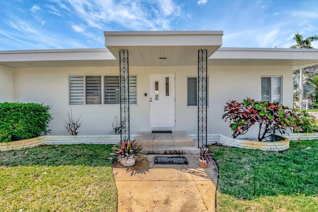 property entrance featuring a yard, covered porch, and stucco siding