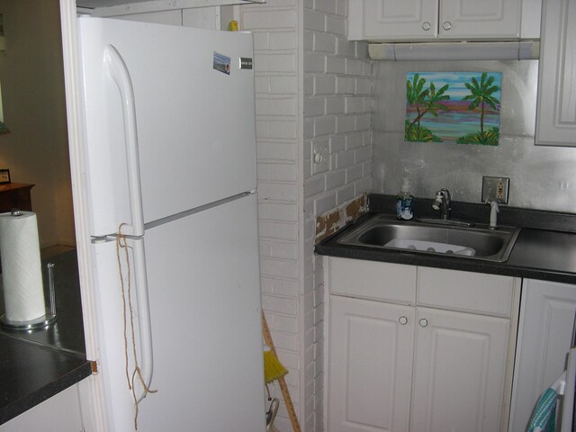 kitchen with dark countertops, freestanding refrigerator, and a sink