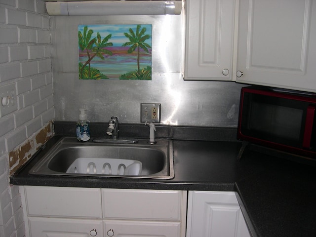 kitchen with dark countertops, white cabinetry, and a sink