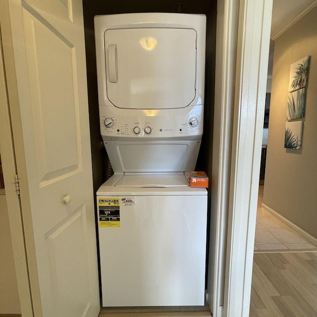 clothes washing area with laundry area, baseboards, stacked washer / drying machine, and light wood finished floors