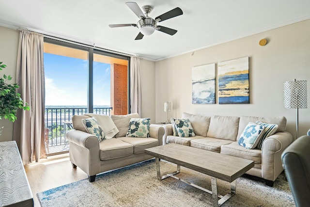 living room featuring light wood-type flooring, ornamental molding, a ceiling fan, and expansive windows