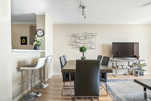 dining space with crown molding, wood finished floors, baseboards, and track lighting