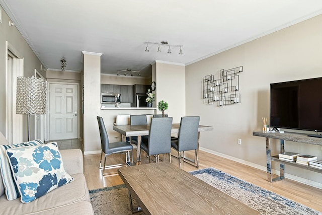 dining room with rail lighting, baseboards, wood finished floors, and crown molding