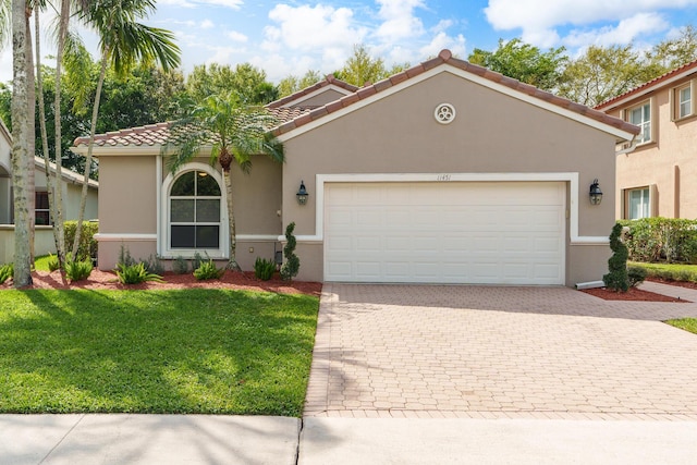 mediterranean / spanish house featuring a tiled roof, a front yard, stucco siding, decorative driveway, and an attached garage