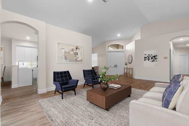 living room featuring light wood finished floors, baseboards, arched walkways, and vaulted ceiling