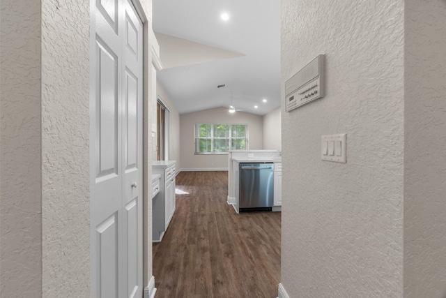 corridor with vaulted ceiling, dark wood-type flooring, baseboards, and a textured wall