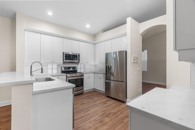 kitchen with light wood finished floors, a peninsula, arched walkways, stainless steel appliances, and a sink