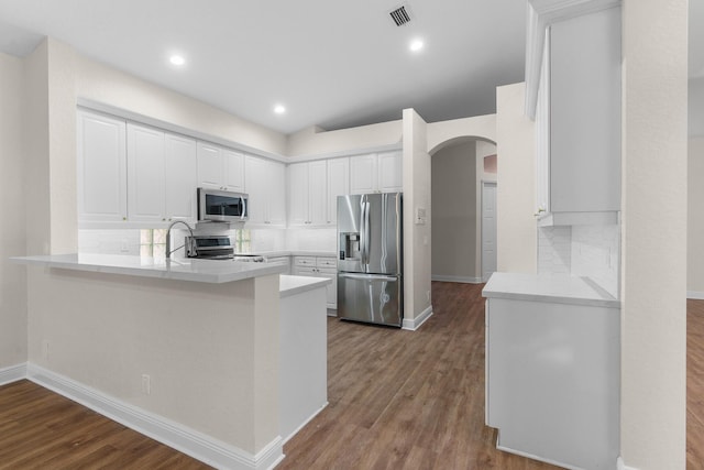 kitchen featuring visible vents, dark wood-type flooring, stainless steel appliances, arched walkways, and decorative backsplash