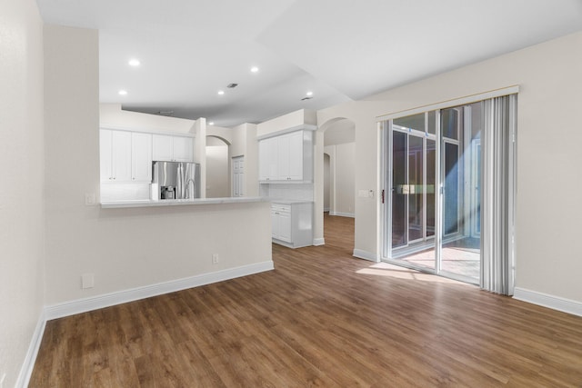 unfurnished living room featuring recessed lighting, wood finished floors, arched walkways, and baseboards