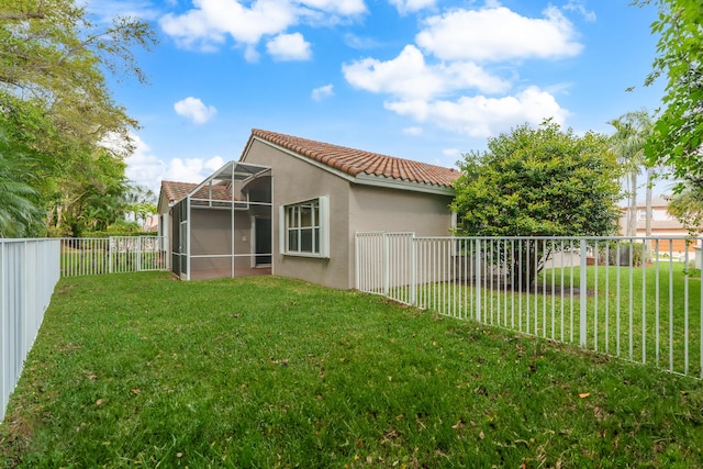 back of house featuring stucco siding, a tile roof, glass enclosure, and a lawn