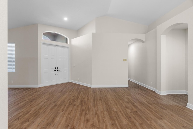 unfurnished room featuring lofted ceiling, wood finished floors, arched walkways, and baseboards