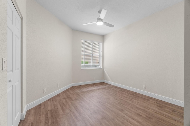 unfurnished bedroom with a textured wall, a ceiling fan, baseboards, and wood finished floors