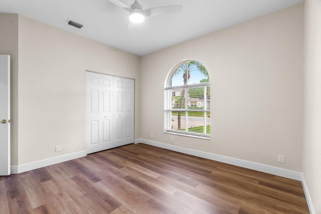 unfurnished bedroom featuring wood finished floors, visible vents, baseboards, ceiling fan, and a closet