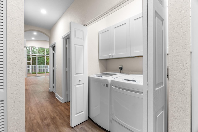 laundry area featuring dark wood finished floors, cabinet space, separate washer and dryer, arched walkways, and a textured wall