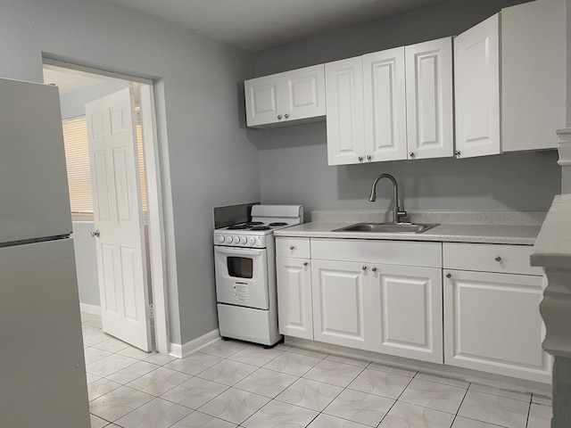 kitchen with a sink, white gas range oven, white cabinetry, freestanding refrigerator, and light countertops