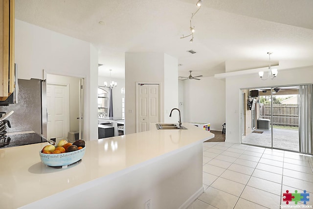 kitchen featuring light tile patterned floors, a peninsula, freestanding refrigerator, hanging light fixtures, and a sink