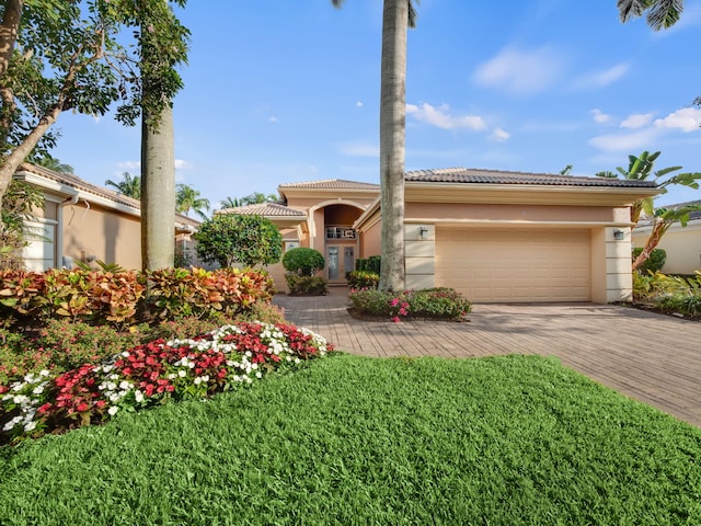 mediterranean / spanish-style house with an attached garage, stucco siding, a front lawn, a tile roof, and decorative driveway