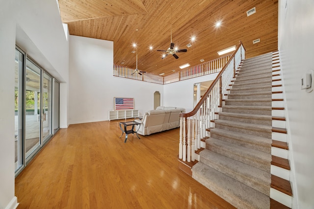 interior space with stairs, wooden ceiling, a high ceiling, wood finished floors, and a ceiling fan