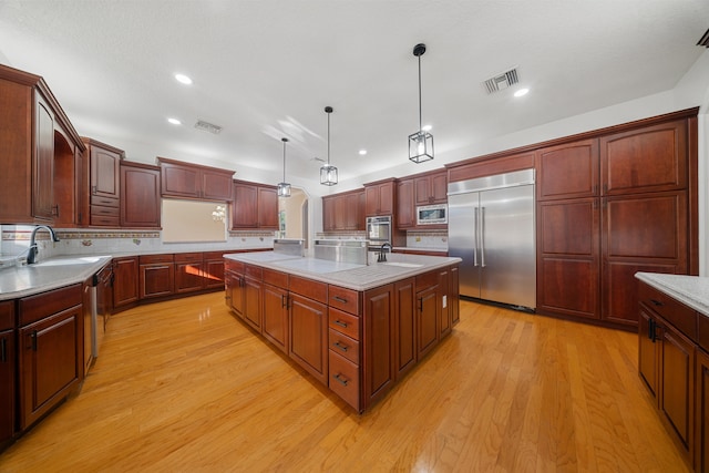 kitchen with a sink, visible vents, built in appliances, and light wood finished floors