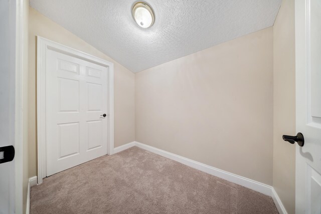 unfurnished room with vaulted ceiling, carpet, baseboards, and a textured ceiling