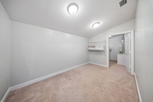 interior space with carpet, baseboards, visible vents, vaulted ceiling, and a textured ceiling