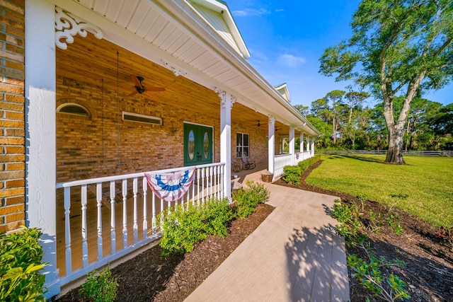 entrance to property featuring fence, a porch, a yard, ceiling fan, and brick siding