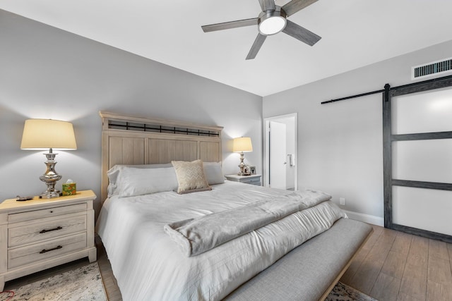 bedroom featuring a ceiling fan, baseboards, visible vents, light wood-style flooring, and a barn door