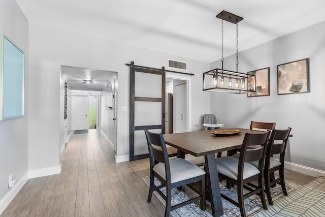 dining room with a barn door, baseboards, visible vents, and wood finished floors