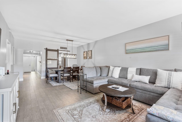 living room featuring light wood-type flooring, baseboards, visible vents, and a chandelier