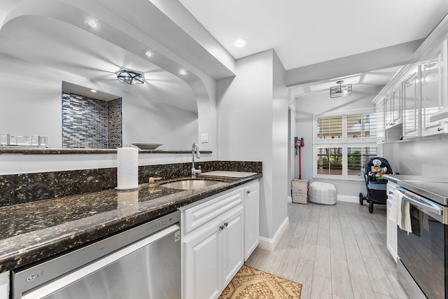 kitchen featuring dark stone countertops, a sink, stainless steel appliances, light wood-style floors, and white cabinetry