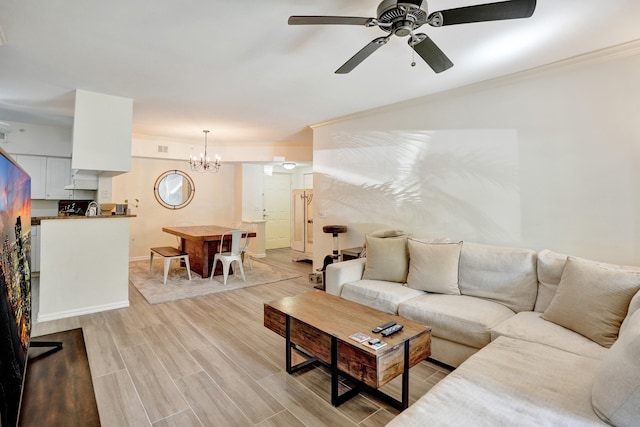 living area with light wood-style flooring, ceiling fan with notable chandelier, baseboards, and ornamental molding