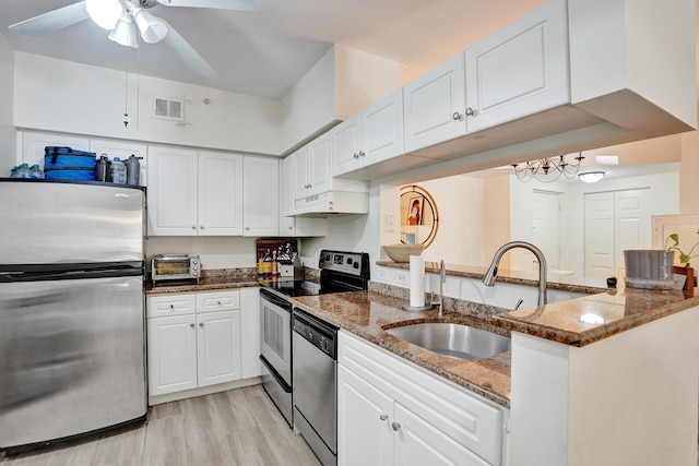 kitchen featuring visible vents, dark stone counters, stainless steel appliances, white cabinetry, and a sink