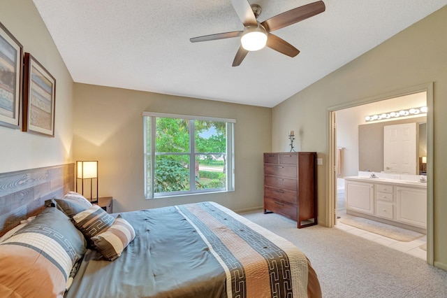 bedroom featuring a ceiling fan, vaulted ceiling, ensuite bathroom, a textured ceiling, and light colored carpet