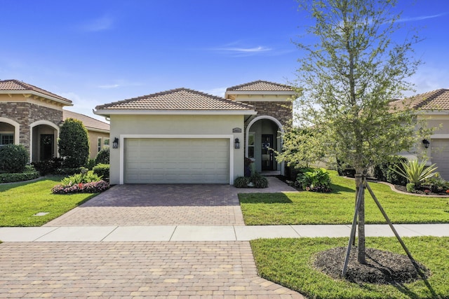 mediterranean / spanish house with stucco siding, decorative driveway, an attached garage, a front yard, and a tiled roof