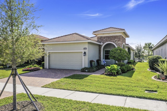 mediterranean / spanish house with stucco siding, decorative driveway, stone siding, a front yard, and an attached garage