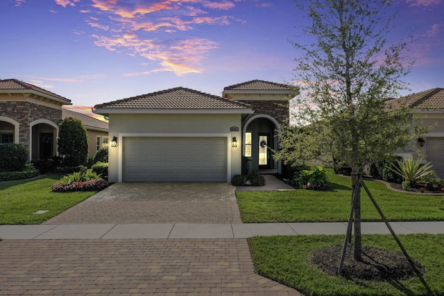 mediterranean / spanish house with a front yard, an attached garage, stucco siding, a tile roof, and decorative driveway