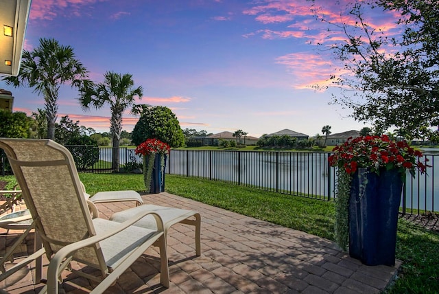 patio terrace at dusk featuring a yard, a fenced backyard, and a water view