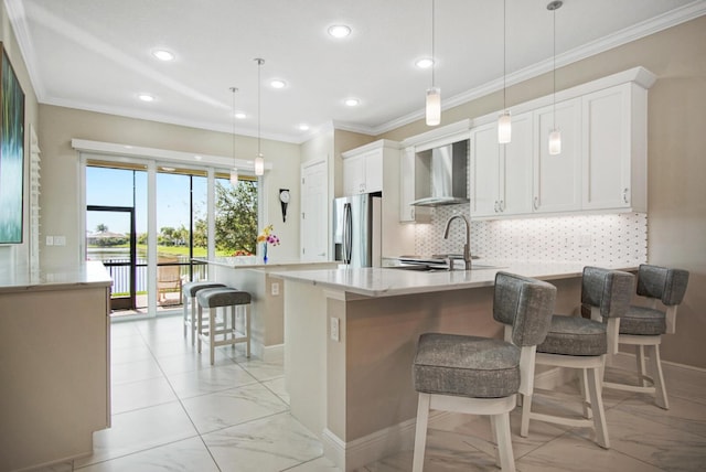 kitchen featuring tasteful backsplash, crown molding, wall chimney range hood, a peninsula, and stainless steel fridge