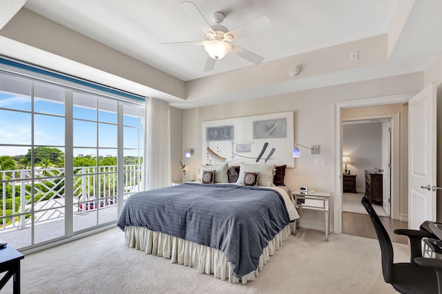 bedroom with a raised ceiling, light colored carpet, access to exterior, and a ceiling fan