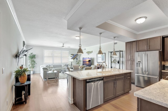 kitchen with a sink, decorative light fixtures, stainless steel appliances, light wood-style floors, and crown molding