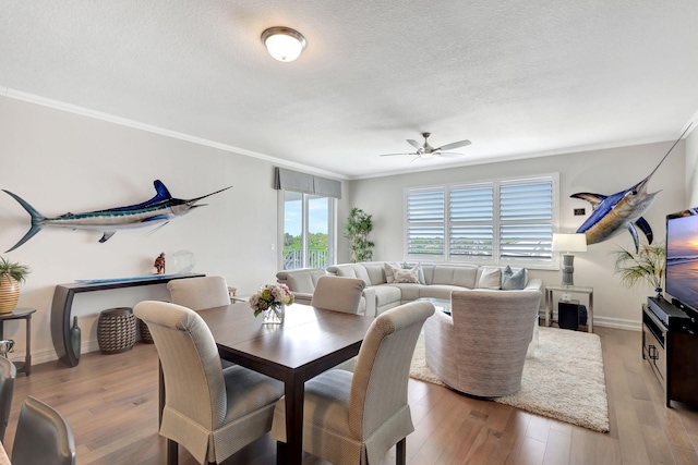 dining space with light wood-style flooring, a textured ceiling, crown molding, and baseboards