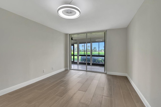 unfurnished room featuring floor to ceiling windows, baseboards, and wood finished floors