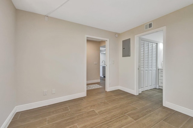 empty room featuring electric panel, visible vents, baseboards, and wood tiled floor