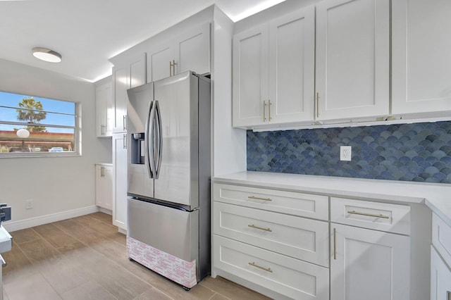 kitchen with tasteful backsplash, white cabinetry, stainless steel fridge, light countertops, and baseboards