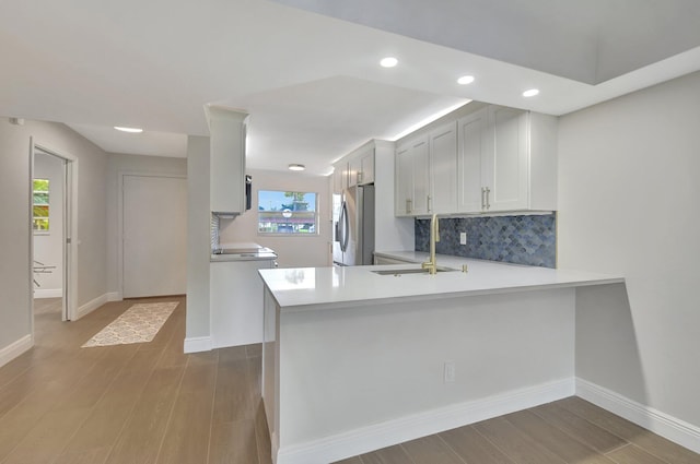 kitchen with wood finished floors, stainless steel fridge with ice dispenser, a sink, light countertops, and backsplash