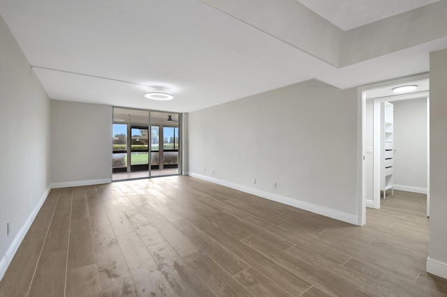 spare room featuring a wall of windows, baseboards, and wood finished floors