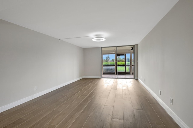 spare room with a ceiling fan, a wall of windows, baseboards, and dark wood-style flooring