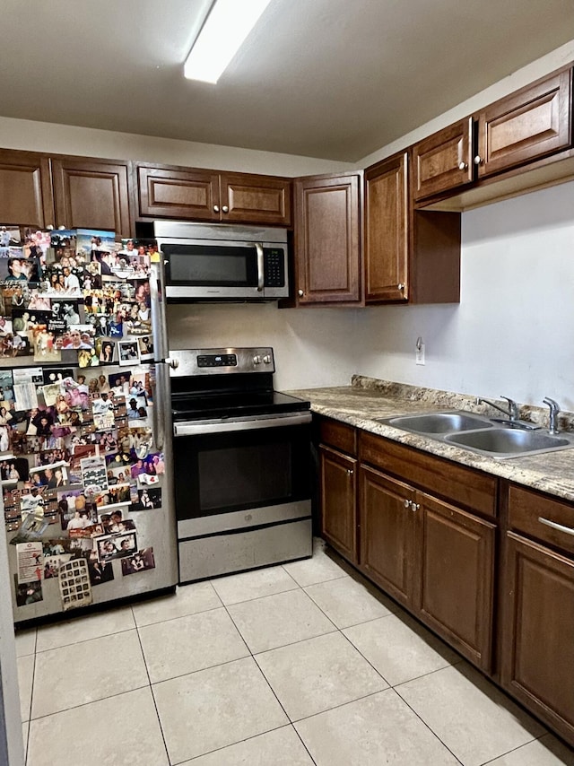 kitchen with a sink, stainless steel appliances, dark brown cabinetry, light countertops, and light tile patterned floors