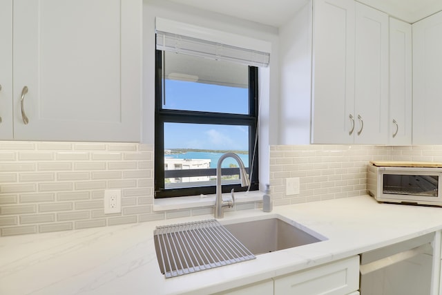 kitchen featuring light stone counters, a toaster, a sink, decorative backsplash, and white cabinets