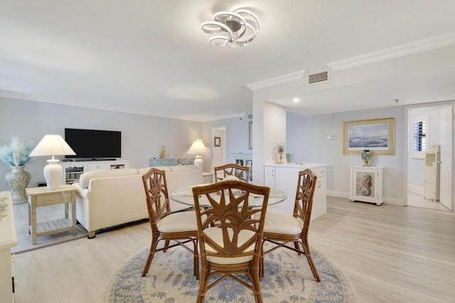 dining room featuring light wood-style flooring, baseboards, visible vents, and ornamental molding